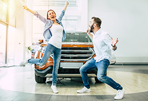 Happy couple at the dealer in front of a new car.