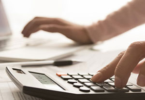 A person typing on keyboard with a calculator